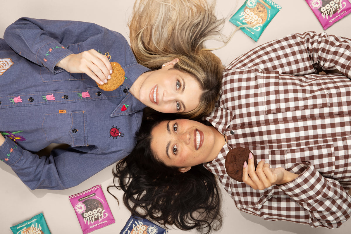 Fields Good co-founders lying on a floor with cookies and packages of cookies around them.
