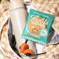 Protein cookie package with a water bottle and earbuds on a checkered blanket