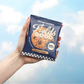 Hand holding a 'Fields Good' cookie package against a cloudy sky background