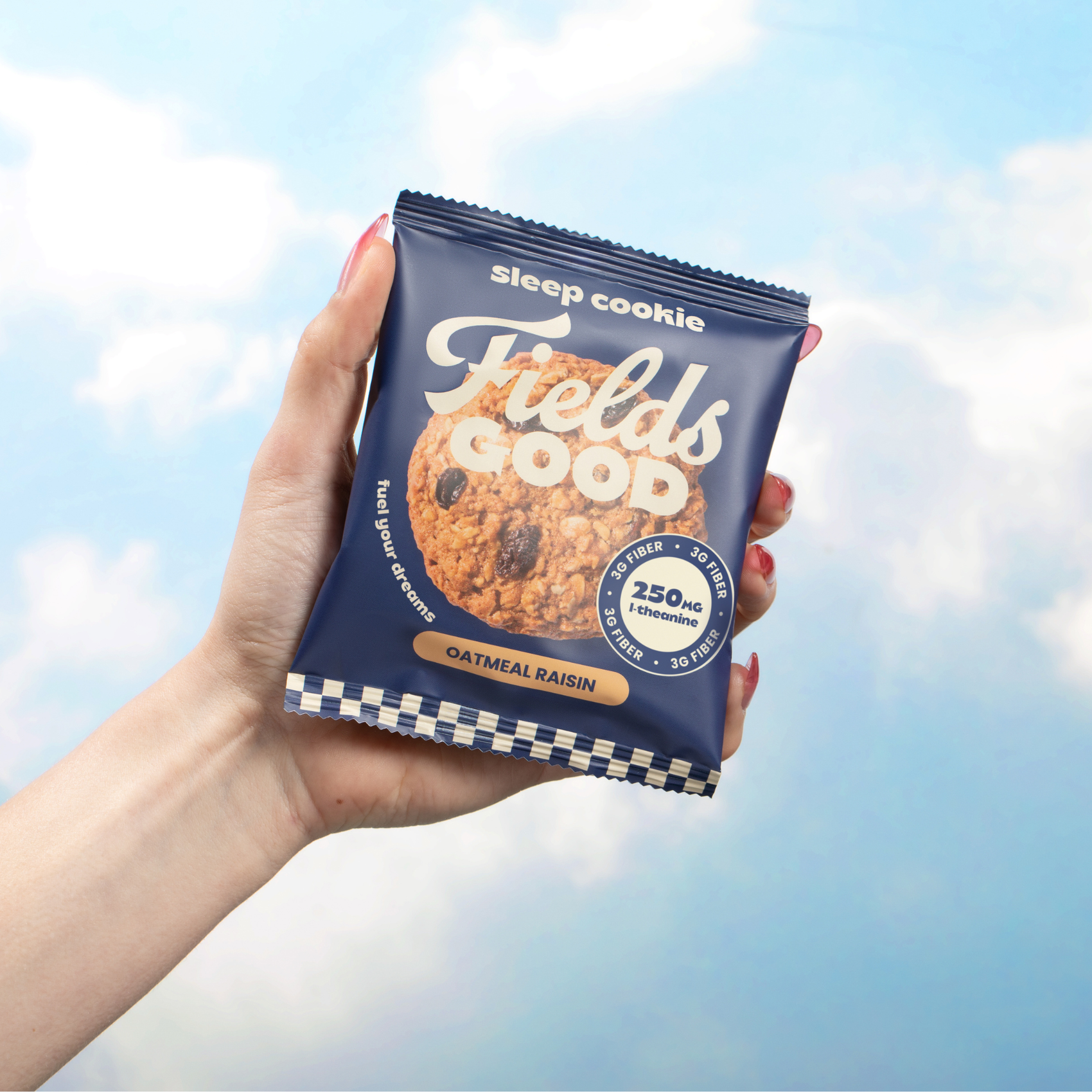 Hand holding a 'Fields Good' cookie package against a cloudy sky background