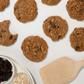 Oatmeal raisin cookies on a white surface with a wooden spatula and ingredients.